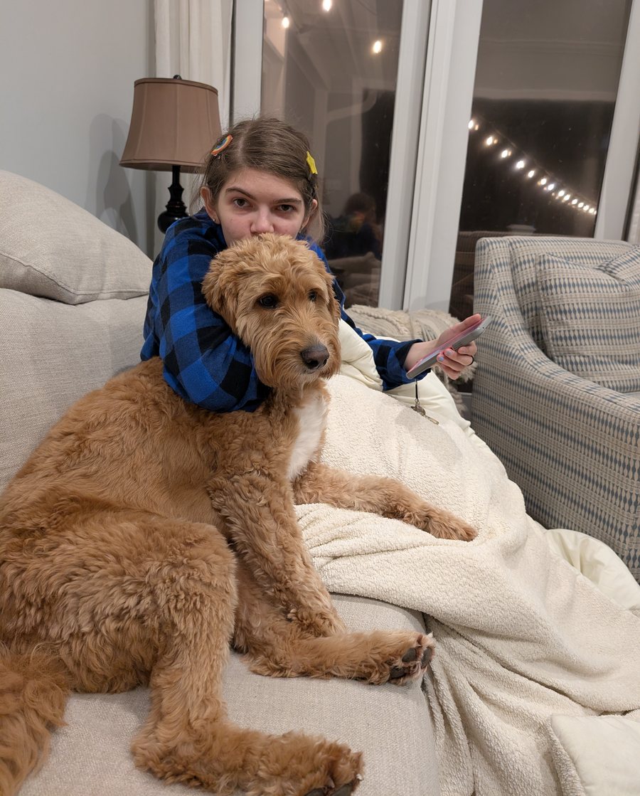 Elisabeth with her arms around a golden doodle on the couch in the evening.