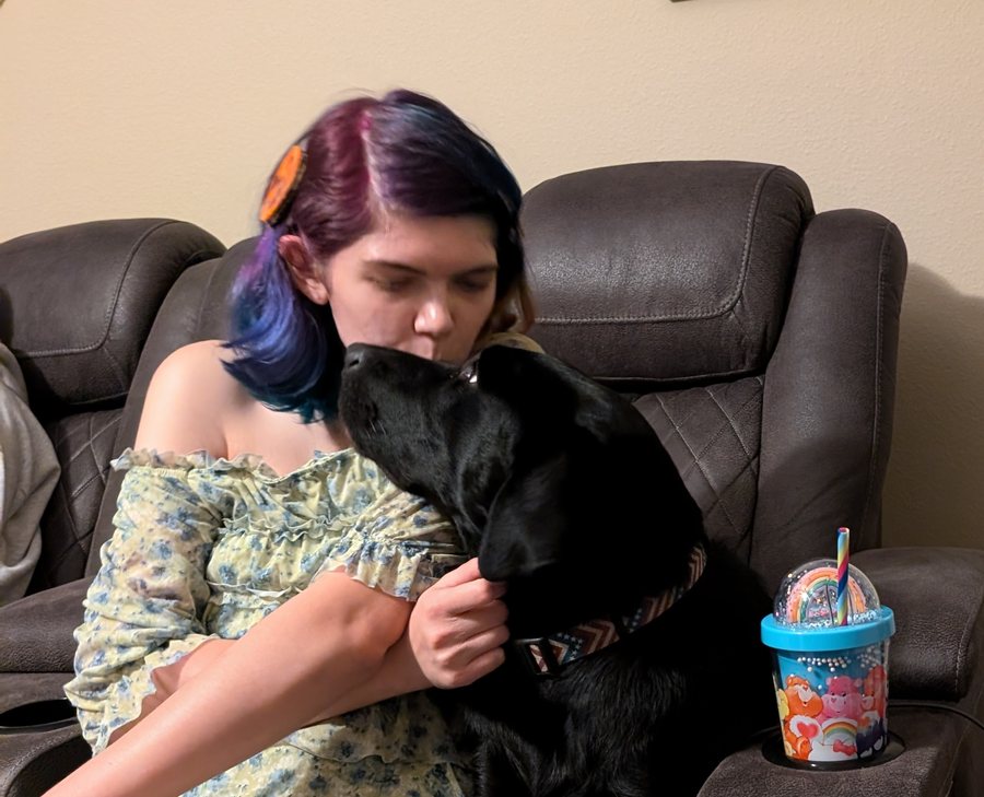 Elisabeth leaning down to kiss a black labrador in an armchair.