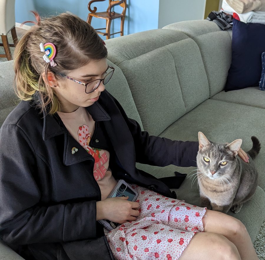Elisabeth sitting on a couch petting a grey tabby cat beside her.